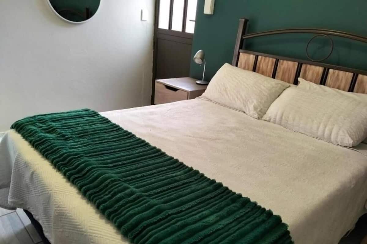 Ein Bett mit einer grün-weißen Decke, einem hölzernen Kopfteil und einem Nachttisch mit einer Lampe.