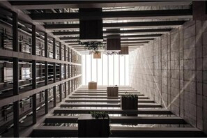 Interior de biblioteca moderna com estantes, escadaria central e plantas penduradas.