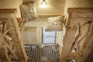 Eine Holzhütte mit einem Netzbett aus Seil, Holzwänden und einer hängenden Leuchte.