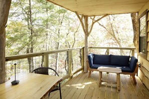 Une terrasse en bois avec un canapé et une table, entourée d’arbres.