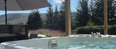 Un jacuzzi con un techo de madera, rodeado de árboles y vista a la montaña.
