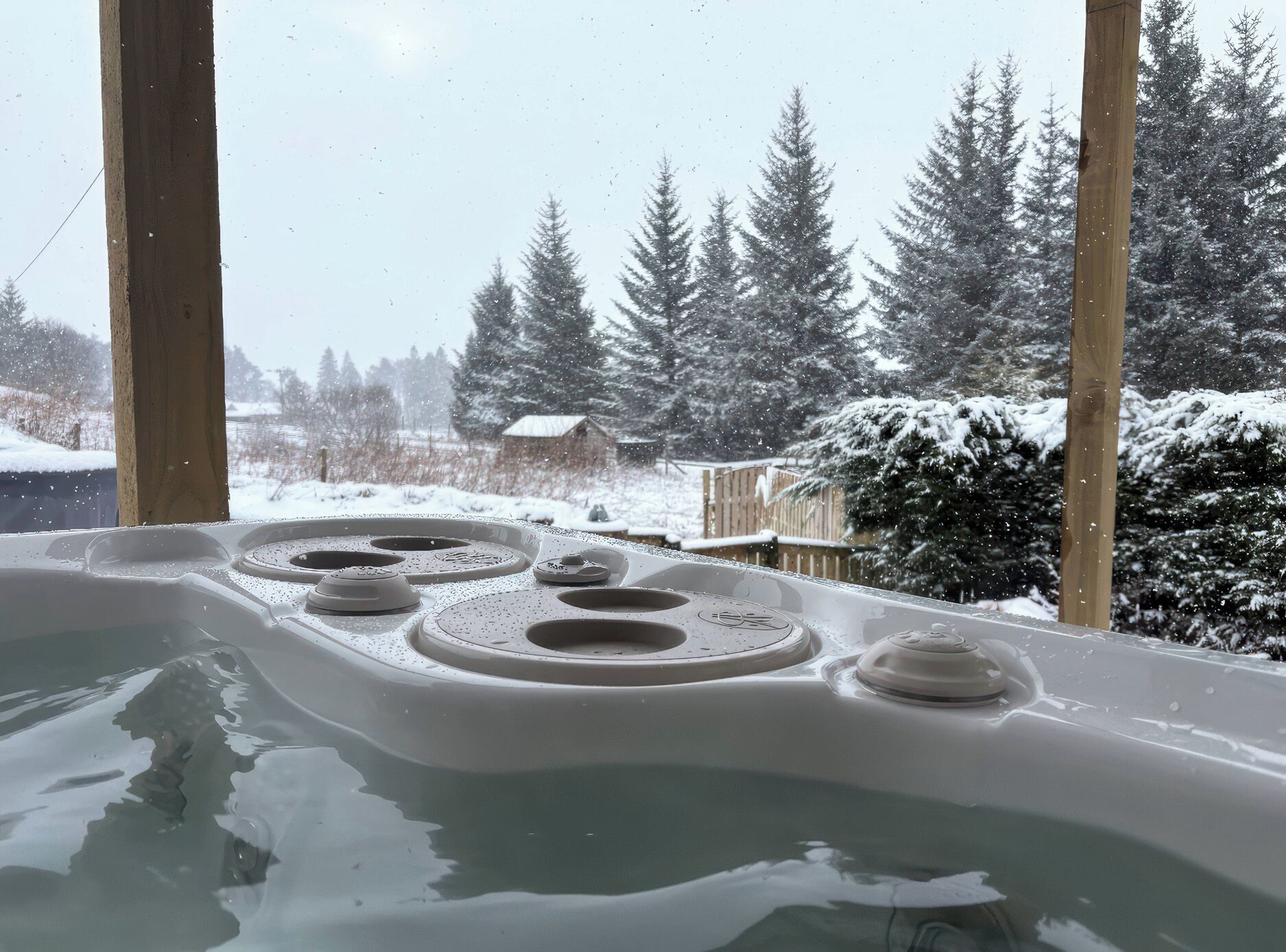 A hot tub with a snowy landscape view, wooden pillars, and a wooden deck.