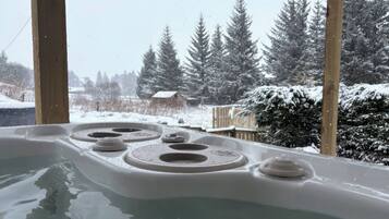 A hot tub with a snowy landscape view, wooden pillars, and a wooden deck.