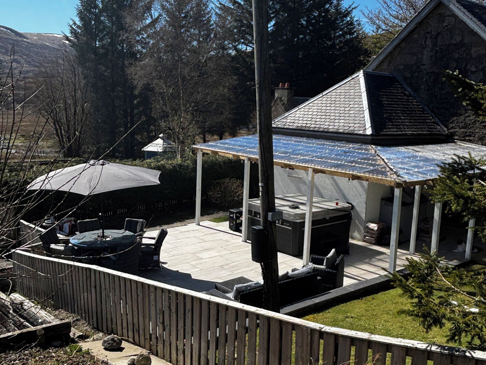 A covered patio with outdoor furniture, a wooden fence, and a house with a sloped roof.