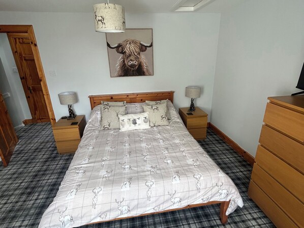 Un dormitorio con una cama, dos mesitas de noche, un aparador de madera, una lámpara y un cuadro de un toro colgado en la pared.