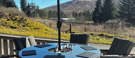 A round outdoor table with chairs, a table umbrella, and bottles of beer.