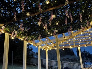 Una pérgola de madera con luces de cuerda y flores moradas.