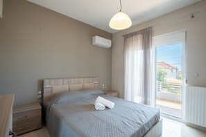 Ein Schlafzimmer mit Bett, Nachttischen, einer Klimaanlage, einem Fenster mit Vorhängen und Blick nach draußen.