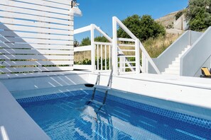 Ein Swimmingpool mit einer Leiter, weißen Geländern und einer Treppe, die zu einer Terrasse führt.