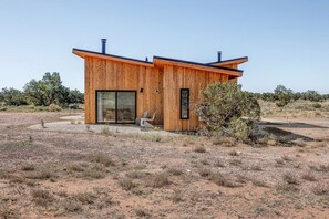 A modern wooden cabin with a large sliding glass door, a small window, and a chair outside. - Eco-Luxury Desert Casita with Private Patio & Stargazing near Grand Canyon, Arizona (Williams)