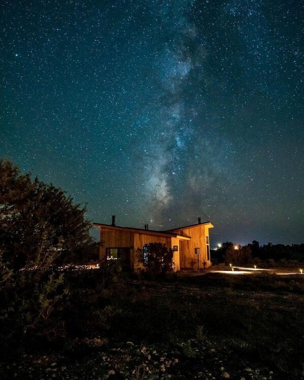 Una baita di legno sotto un cielo stellato con la Via Lattea ben visibile.