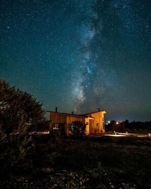 Eine Holzhütte unter einem Sternenhimmel, die Milchstraße ist sichtbar.