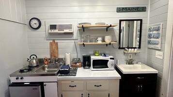 A compact kitchen with a sink, stove, microwave, and a refrigerator. There is a clock on the wall and a sign that says 'MAINE'.