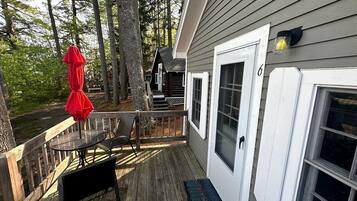 A wooden deck with a table and chairs, a red umbrella, and a door with a number.