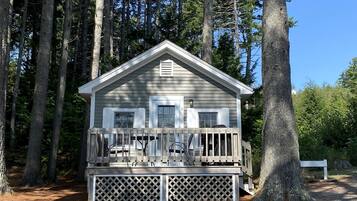 A cabin with a porch, surrounded by tall trees.