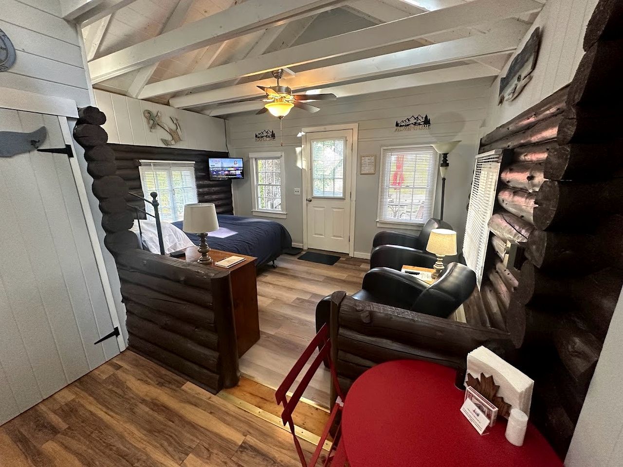 A log cabin interior with a bed, two chairs, a desk, and a television.