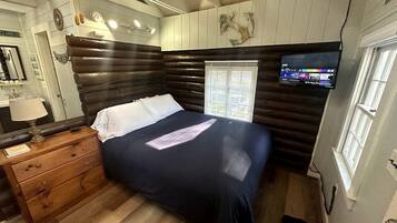A room with a bed, wooden dresser, and a television mounted on the wall.