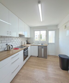 A modern kitchen with white cabinets, a stainless steel dishwasher, and a wooden countertop.