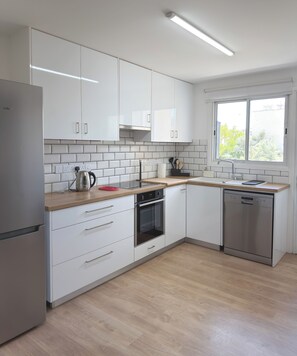 Ett modernt kök med vita skåp, ett kylskåp i rostfritt stål, en inbyggd ugn och en diskmaskin.