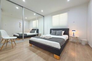 A modern bedroom with a large bed, bedside tables, a chair, and a mirror.