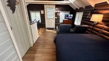 Interior de una cabaña de troncos con una cama, un escritorio y un televisor.