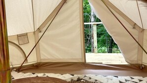 Una tenda con vista sul verde circostante, sgabelli di legno e un tappeto tessuto all'interno.