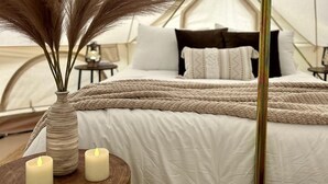 Un alloggio in tenda con un letto, un vaso con piante secche e due candele accese su un tavolo di legno.