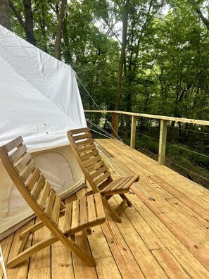 Une terrasse en bois avec une tente blanche et deux chaises en bois.