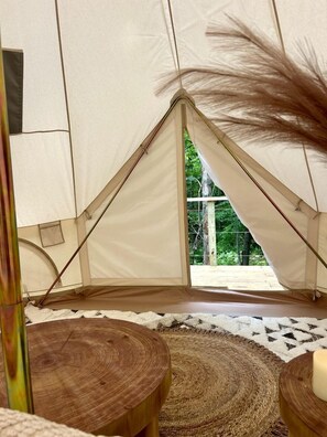 Une tente offrant une vue sur la verdure environnante, des tabourets en bois et un tapis tissé à l’intérieur.