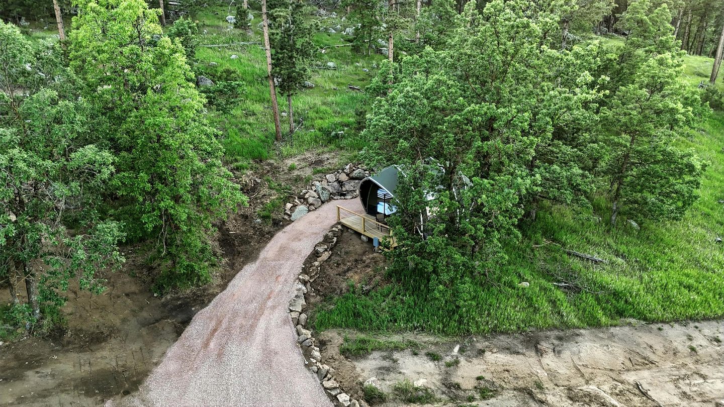 Un camino estrecho y sinuoso que atraviesa un bosque, con un pequeño puente y una pasarela de madera.