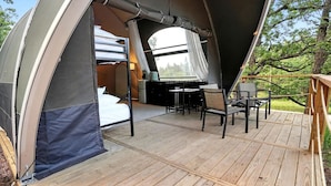 Une tente équipée d’un lit, d’un bureau et de chaises, installée sur une terrasse en bois.