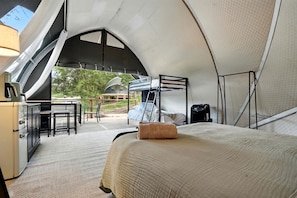 Eine Zelthotelleinheit mit Etagenbett, Schreibtisch, Stühlen und Blick ins Freie.