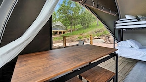 Une tente avec une table en bois et des lits superposés, une vue sur l’extérieur et un espace abrité doté d’une rambarde.