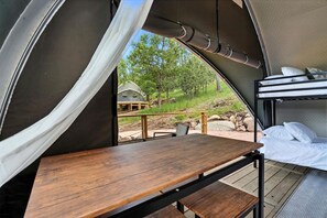 Uma tenda com mesa de madeira e beliches, vista para o exterior e área coberta com corrimão.