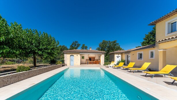 Una piscina amb gandules, un edifici amb teulada ceràmica i un cel blau clar.