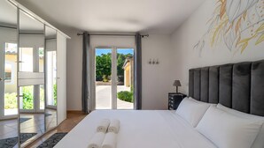 Habitació d'hotel amb un llit, una taula de nit, una làmpada, una finestra gran amb vistes i una porta corredissa que dona a una zona exterior.