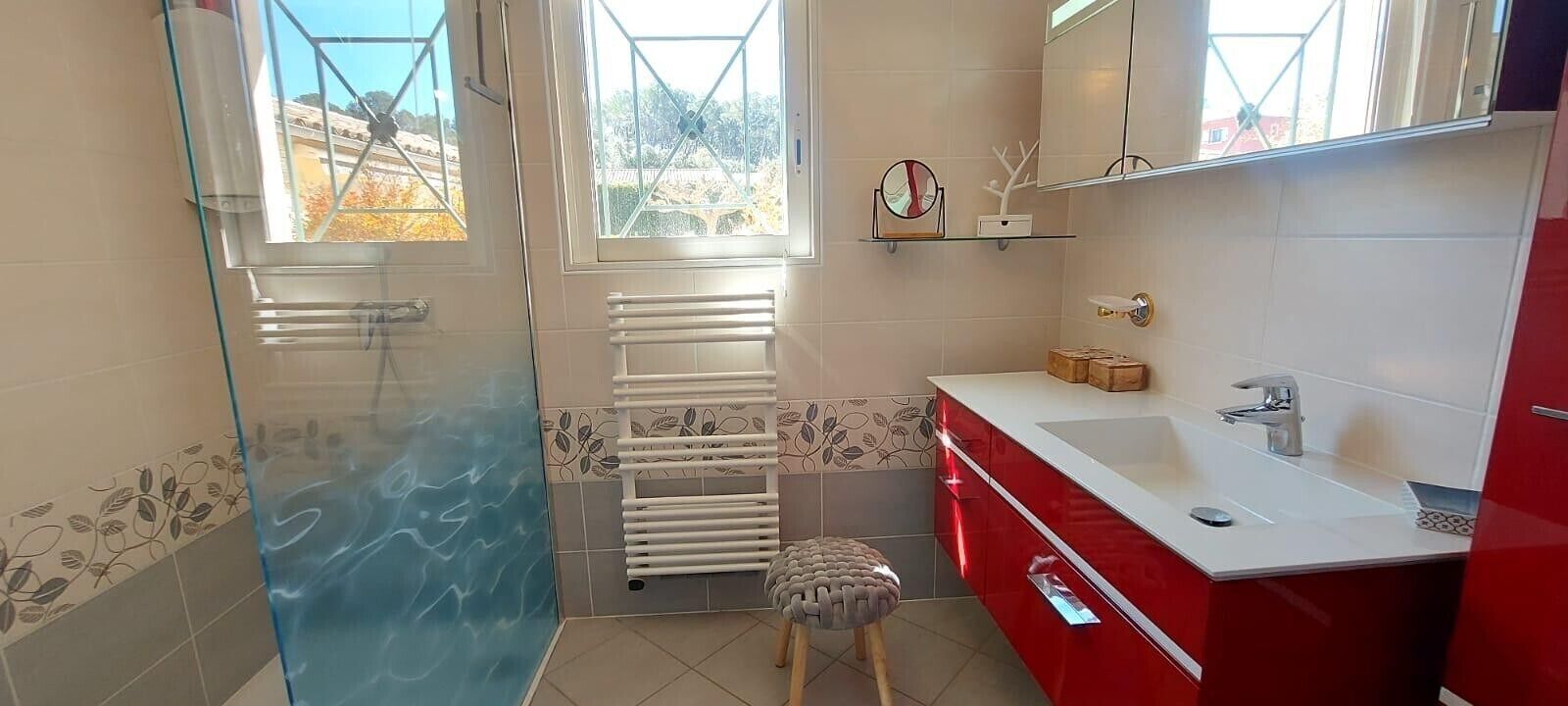 A bathroom with a glass shower enclosure, a white towel rack, a red vanity with a sink, and a mirror.