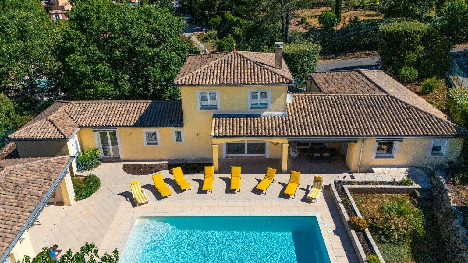 A large house with a swimming pool, multiple lounge chairs, and a well-maintained garden.