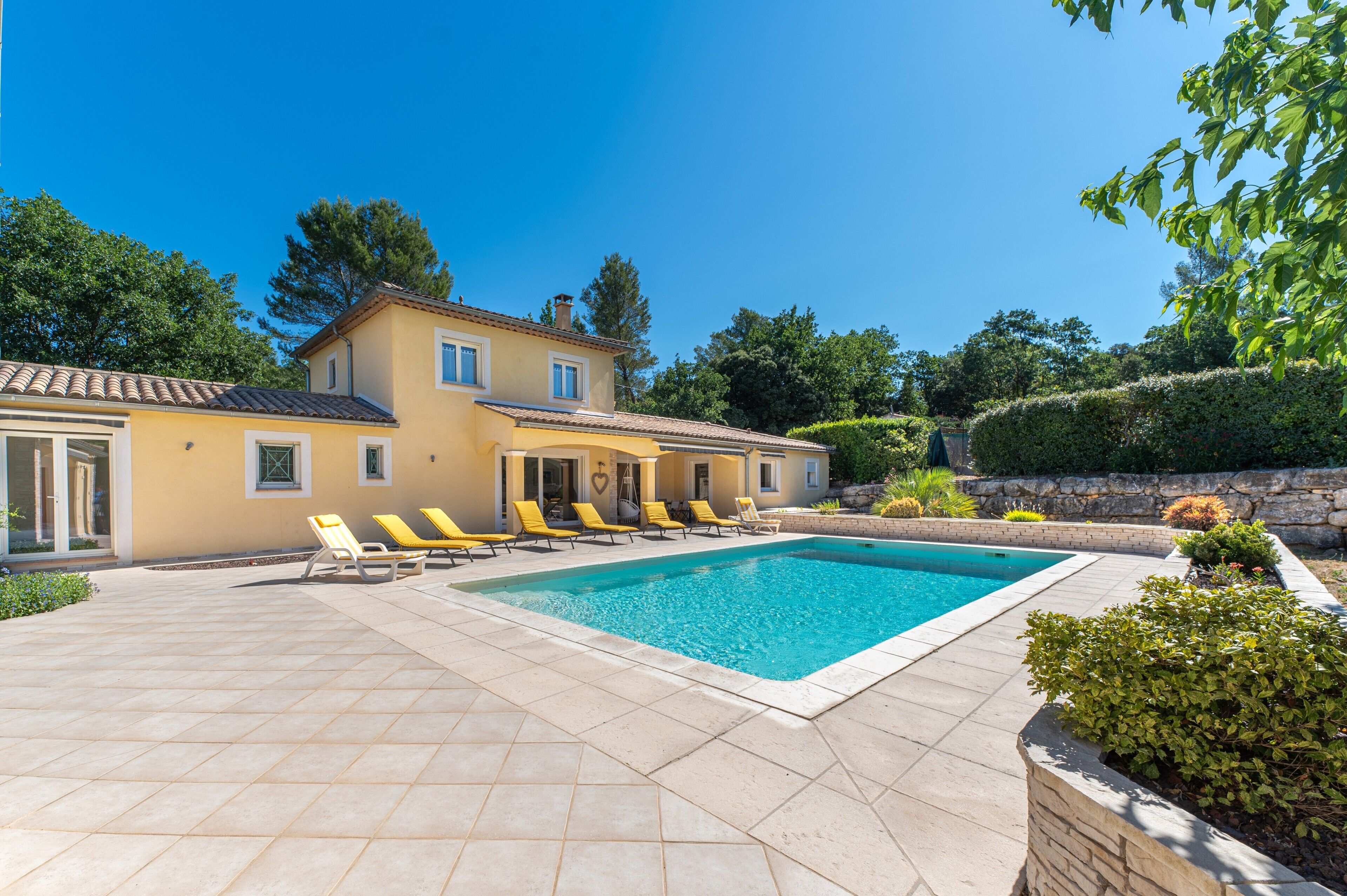 Une piscine avec des chaises longues, une maison et un jardin aménagé.