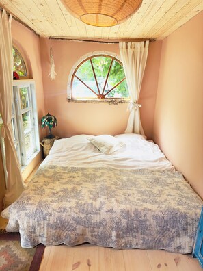 Un dormitorio con cama, ventana con cortinas, techo de madera y vistas a zonas verdes.