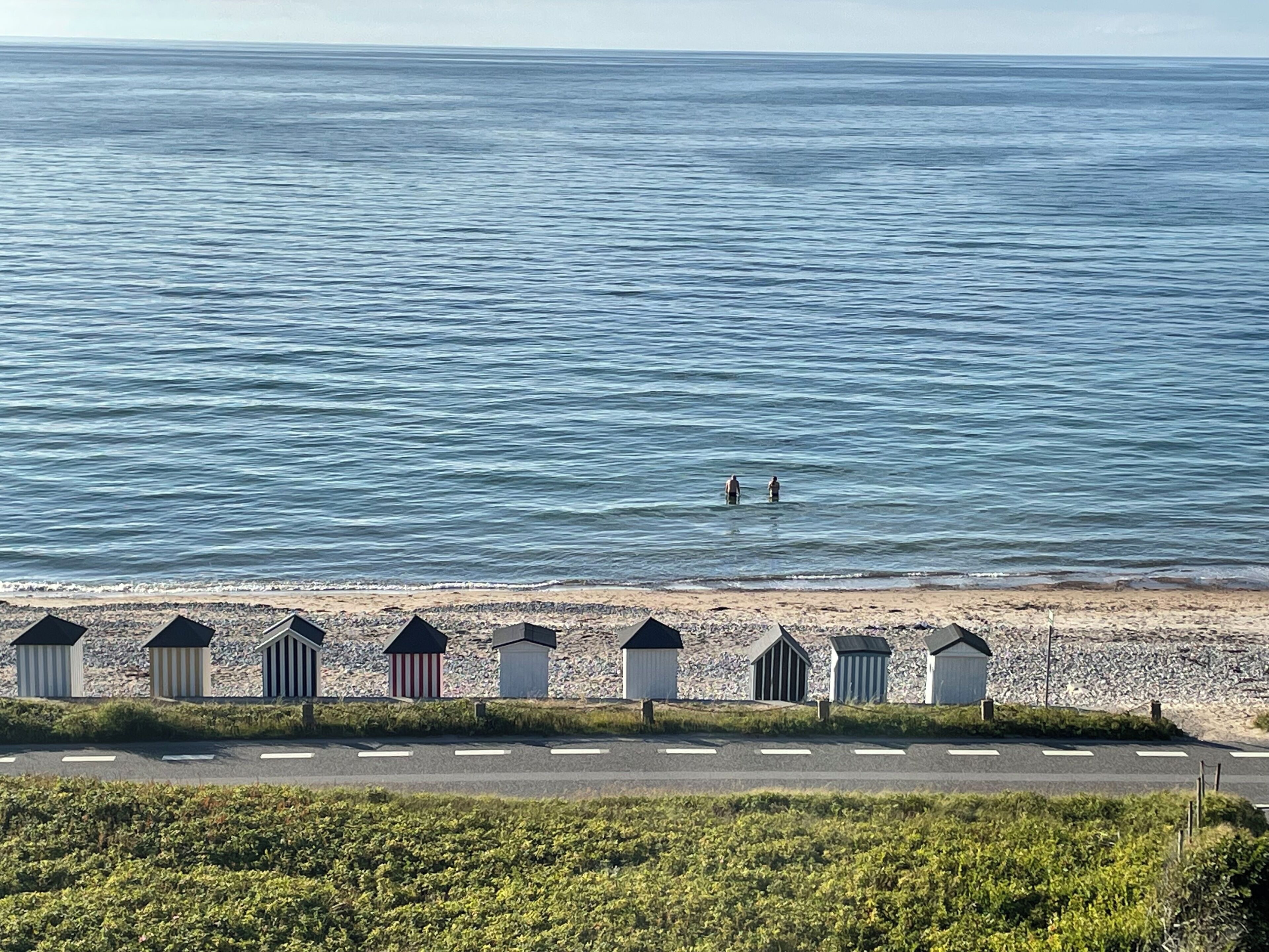 A beach with a row of beach huts and a road in the foreground.