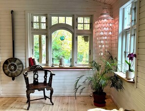 A room with a wooden bench, a potted plant, a hanging lamp, and a window with a view of greenery. - Charming Rågeleje Summer House with Sauna (Græsted)