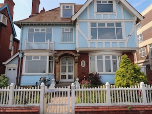 Ein zweistöckiges Haus mit Erkerfenster, Eingangstür und weißem Ziergartenzaun.