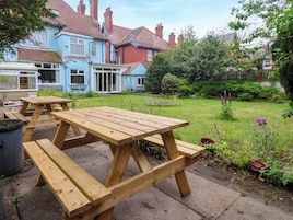 Un juego de mesa de picnic de madera en un jardín, con una casa al fondo.