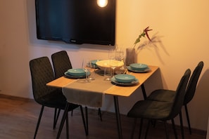 A dining table with chairs, a flat-screen TV mounted on the wall, and a potted plant. - Feniks Apartments (Nessebur)
