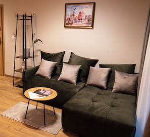 A living room with a sectional sofa, a small round table, and a cityscape painting on the wall.