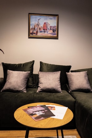 Ein dunkelgrünes Sofa mit drei Kissen, ein runder Holztisch mit einer Zeitschrift und ein gerahmtes Bild darüber.