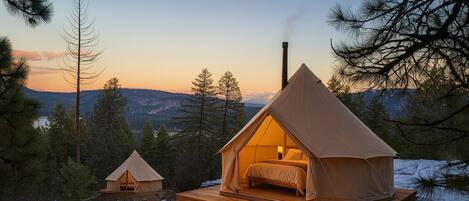 A tent with a bed inside, surrounded by trees and a mountain view.