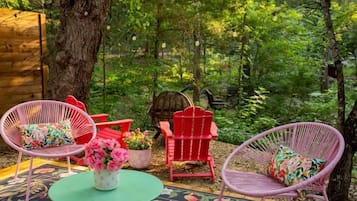 A forested outdoor area with wicker chairs, a small table, and a potted plant.