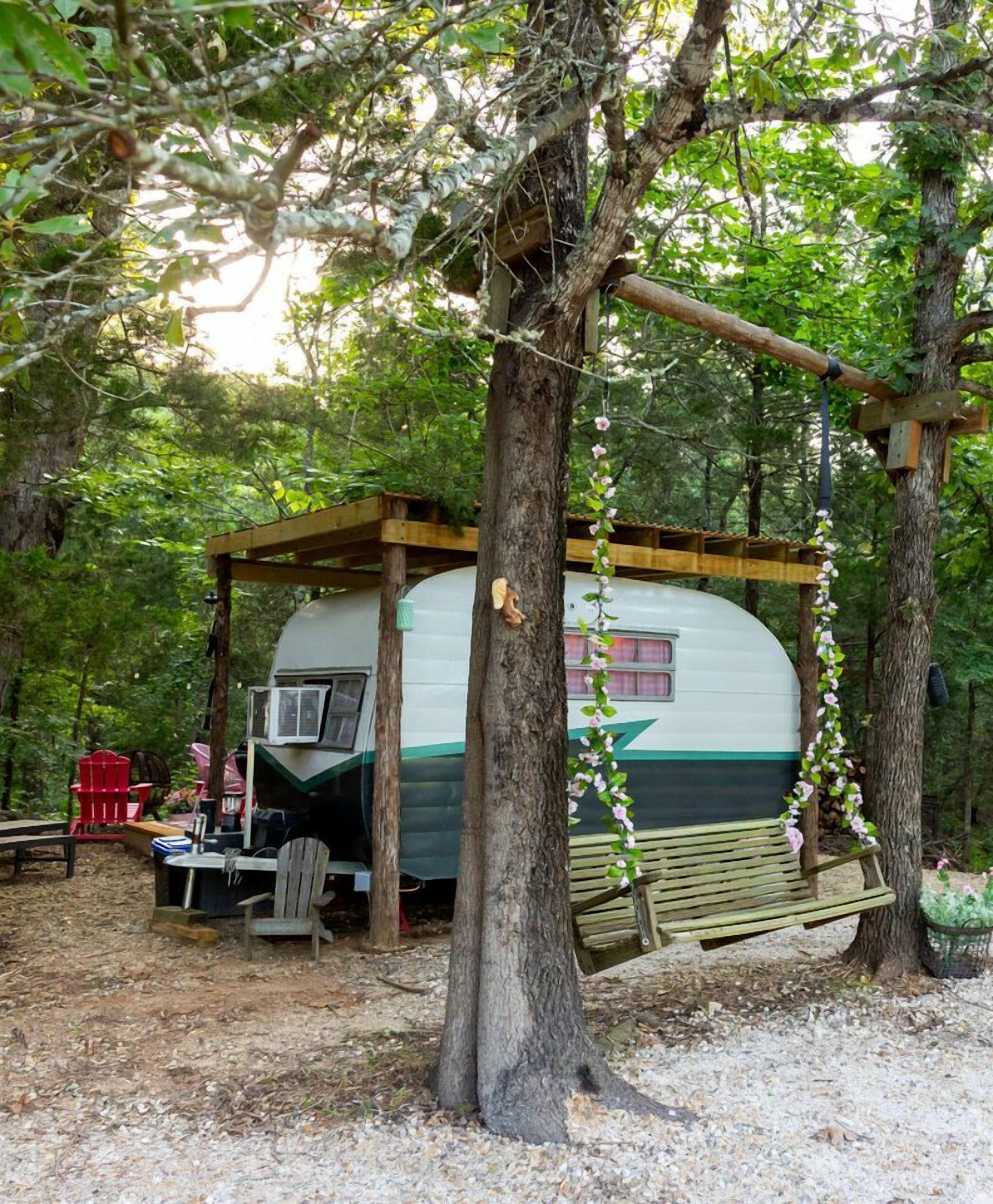 Une cabane de camping dotée d’un porche abrité, d’une balançoire et d’une table avec des chaises.